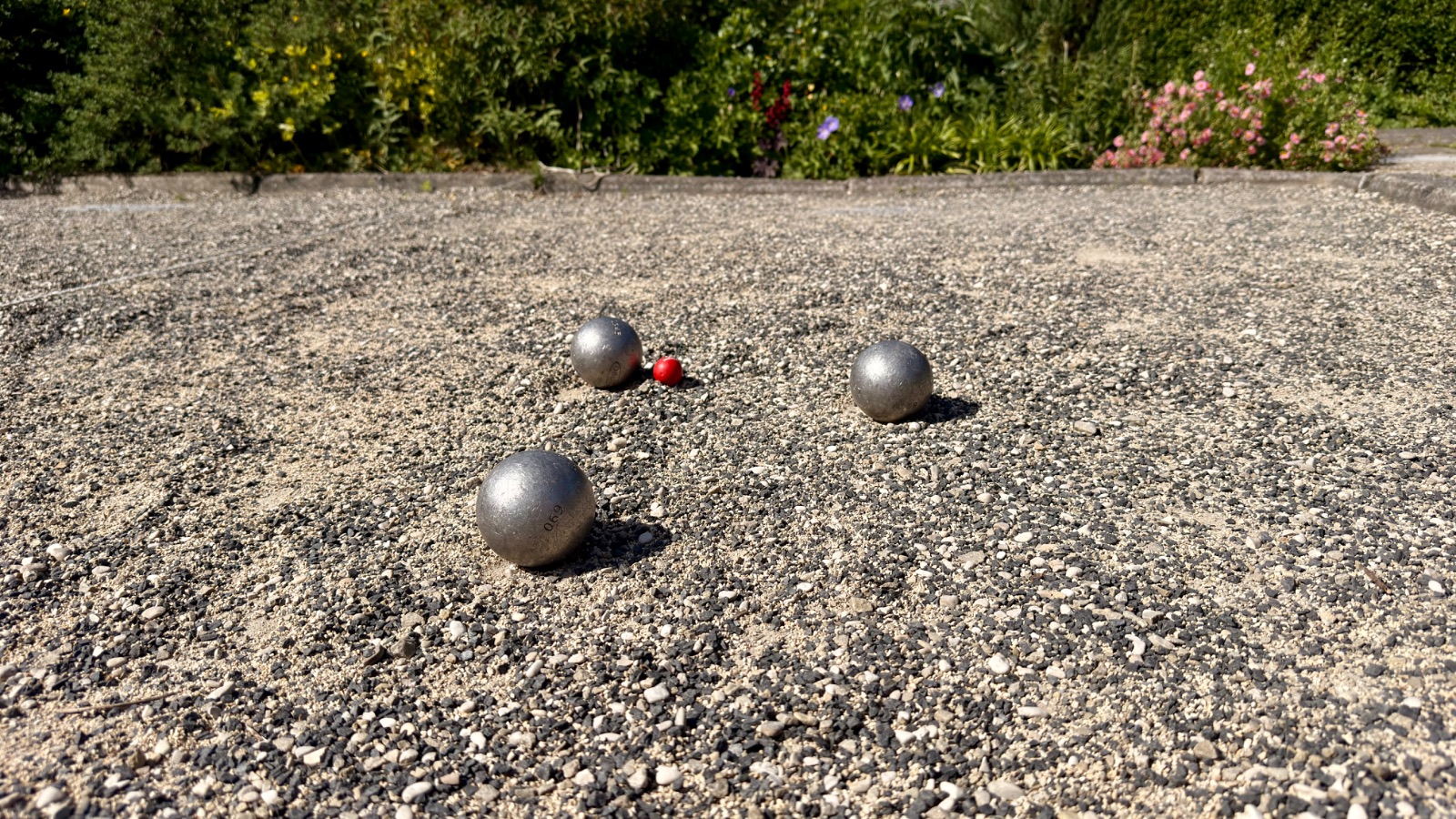Drie boules en het but op een jeu-de-boulesbaan, omzoomd door planten